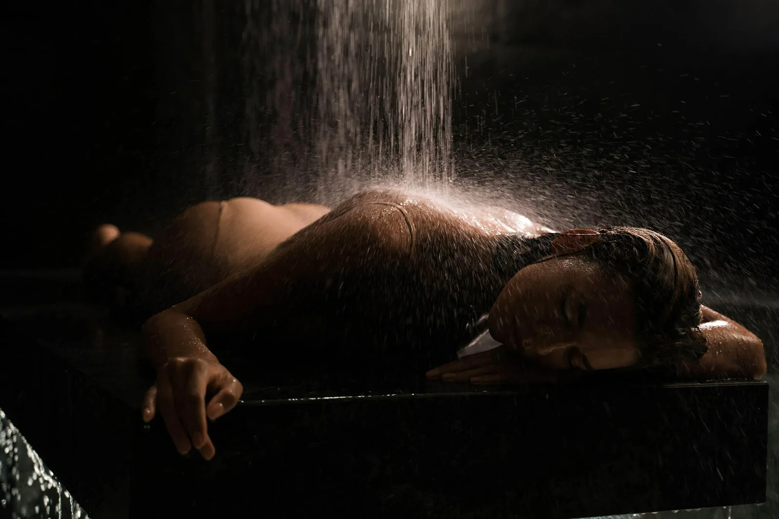 Warm water falling over a woman's shoulders in a dark, quiet room